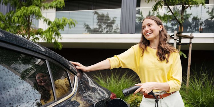 Die neue Förderung für E-Autos in 2026 erlaubt bis zu 4.000 € Prämie Lachende Frau im gelben Pullover lädt ihr E-Auto zuhause
